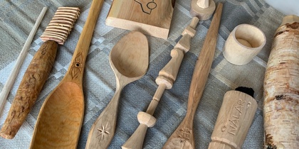 Handgjorda träföremål, som skedar och koppar, ligger på en gråmönstrad duk.