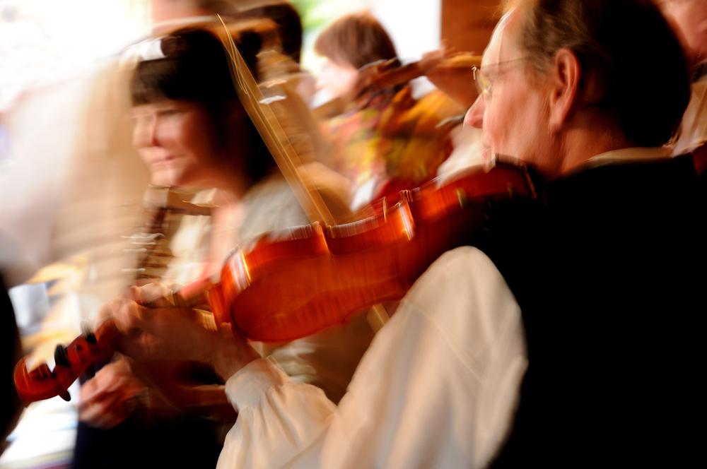 Suddig bild av personer som spelar fiol i en livlig miljö, rörelseoskärpa dominerar.