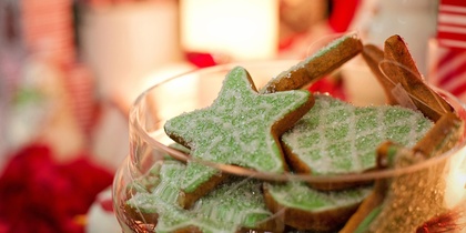 En skål med gröna stjärnformade kakor dekorerade med socker, omgiven av juldekorationer.