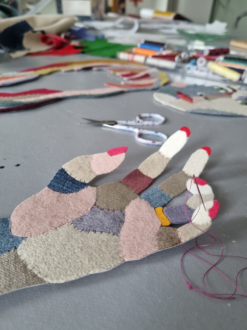 Närbild på en tygapplikation i form av en hand, sydd med färgglada tygbitar och tråd på ett arbetsbord.