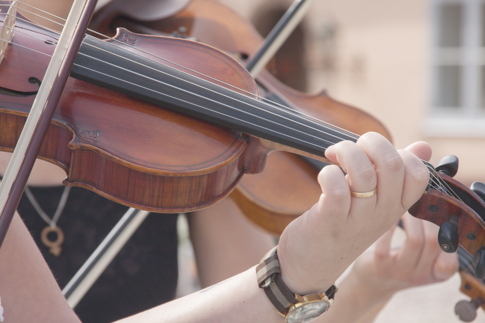 Närbild på en person som spelar fiol utomhus, med fokus på händer och instrument.