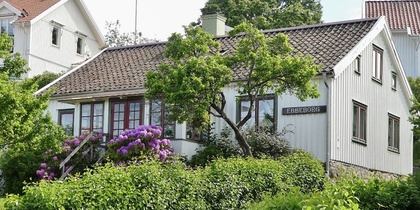 Vit trävilla med blommande buskar och trädgård, sommargrönska och grusgång framför huset.