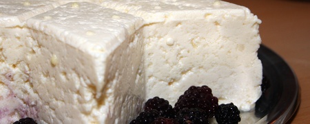 En bit vit ostkaka serverad på ett fat med svarta björnbär bredvid.