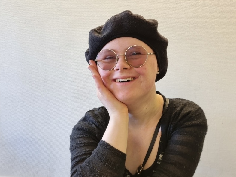 Person med svart basker och svart tröja sitter vid ett bord med ansiktet dolt.