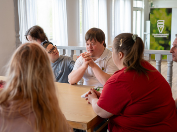 En grupp personer sitter runt ett bord och samtalar i ett ljust rum.