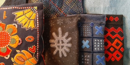 Flera textilier med färgglada broderier och mönster, inklusive kuddar och väskor, visas tillsammans.