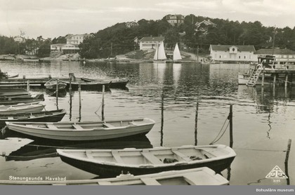 Svartvit bild av småbåtar vid en brygga i Stenungsund, med segelbåtar och hus i bakgrunden.
