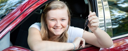 Ung kvinna sitter i en röd bil och håller upp en bilnyckel med ett leende.