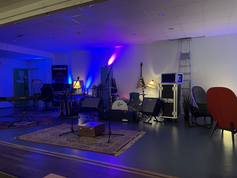 En scen med musikinstrument, mikrofoner och färgad belysning, redo för en konsert eller repetition.