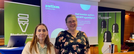 Två kvinnor står framför en presentation om autism i ett konferensrum med gröna och lila färgteman.