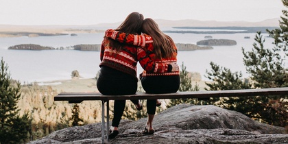 Två personer sitter på en bänk med ryggen mot kameran och ser ut över en sjö och skog.
