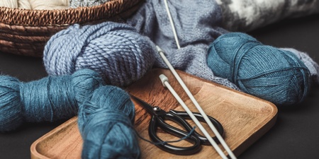 Garnnystan, stickor och sax ligger på en bricka och i en korg, redo för stickning.