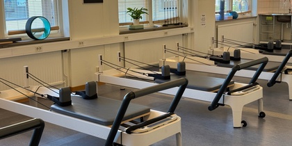 Ett ljust pilatesrum med flera reformermaskiner, stora fönster och träningsredskap på fönsterbrädorna.