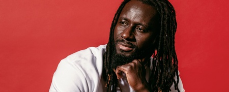 Pa Modou Badjie i vit t-shirt och svarta arbetsbyxor sitter på högtalare mot röd bakgrund