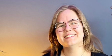 Två leende personer sitter tillsammans i en blå soffa i ett rum med blå vägg och grön växt.