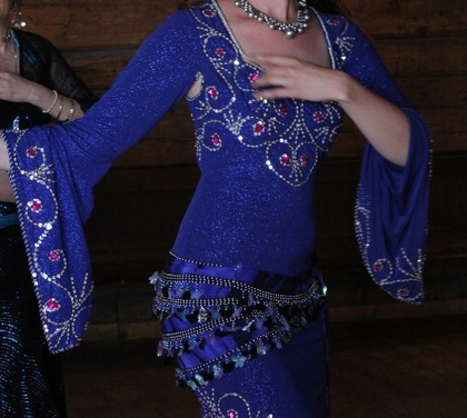 Person i blå glittrande klänning med pärlor och paljetter, dansar inomhus.