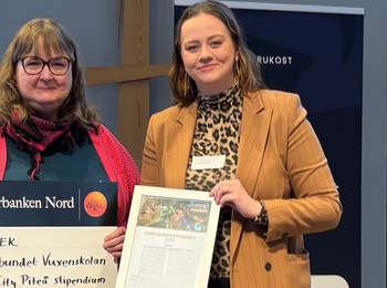 Två personer håller en stor check och ett diplom på en scen med Piteå kommuns logotyp i bakgrunden.