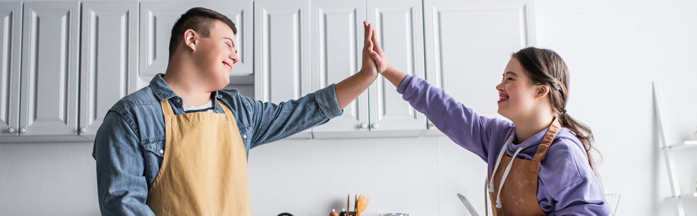 Två unga personer med förkläden ger varandra en high five i ett ljust kök.