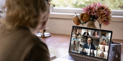 En person deltar i ett videomöte med flera deltagare på en bärbar dator vid ett skrivbord.
