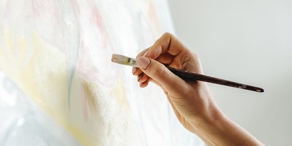 En hand målar på en duk med en pensel, palett med färg syns i förgrunden.