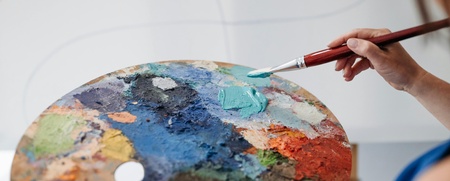 En person håller en pensel och en färgpalett fylld med olika färger, redo att måla.