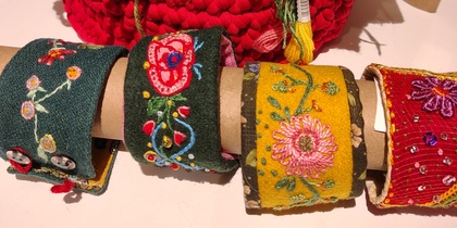 Färgglada handgjorda armband och stickade lappar med broderier och garnnystan på ett bord.