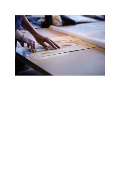 Två händer arbetar med ritningar eller mönster på ett bord i ett ljust rum.