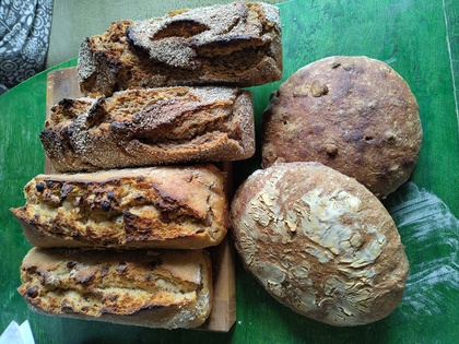 Sex hembakade bröd i olika former ligger på ett grönt bord.