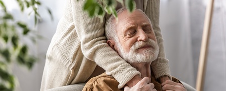 En äldre man sitter i en fåtölj med slutna ögon och ser avslappnad ut medan någon håller om honom bakifrån.