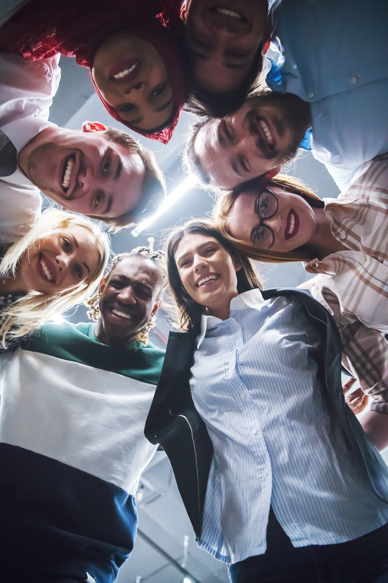 En grupp glada människor står i en cirkel och tittar ner mot kameran, fotograferade underifrån.