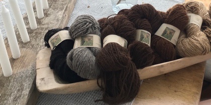 Flera nystan ullgarn i olika naturfärger ligger i en träskål på ett bord.