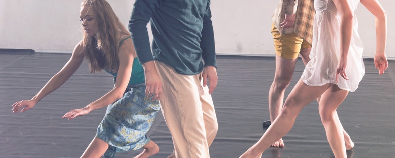 Fyra personer dansar barfota på ett svart golv i en ljus dansstudio.