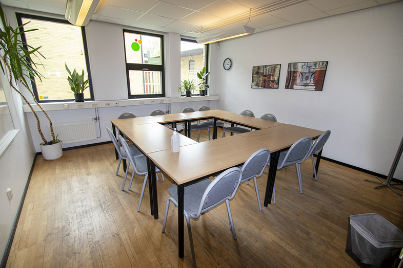 Ett ljust konferensrum med U-formade bord, grå stolar, växter och tavlor på väggen.