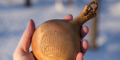 En hand håller en liten, rund träflaska med ingraverat mönster, utomhus i vintrig miljö.