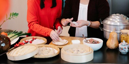 Två personer gör dumplings tillsammans i ett kök, med ingredienser och ångkokare på bordet.
