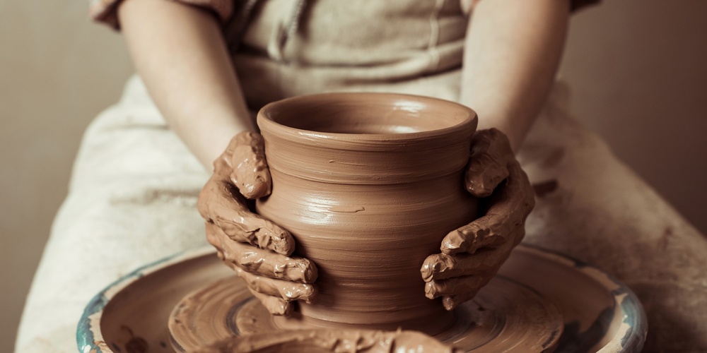 En person formar en lerkruka på en drejskiva med leriga händer.
