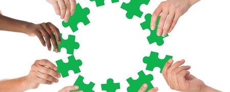 Flera händer håller gröna pusselbitar i en cirkel mot en vit bakgrund.