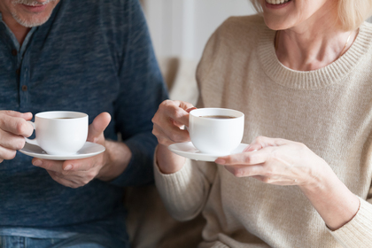 Två personer sitter tillsammans och håller vita kaffekoppar, leende och samtalande.