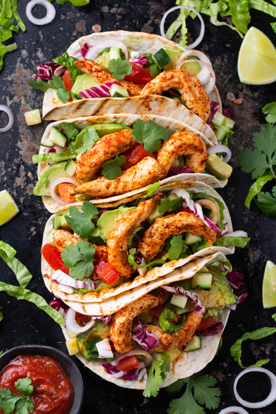 Tre tacos med grillad kyckling, grönsaker och koriander på ett mörkt underlag, med limeklyftor och salsa vid sidan.