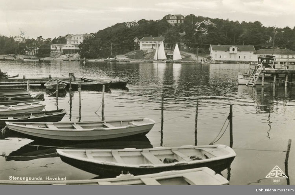 Svartvit bild av småbåtar vid en brygga i Stenungsund, med segelbåtar och hus i bakgrunden.