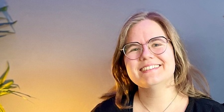 Två leende personer sitter tillsammans i en blå soffa i ett rum med blå vägg och grön växt.