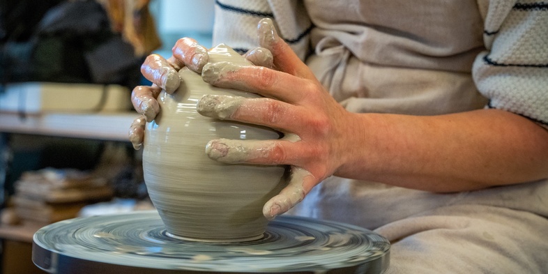 En person formar lera på en drejskiva i en keramikverkstad.