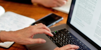 Två personer arbetar vid ett träbord med en laptop, anteckningsbok och penna.
