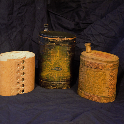 Tre dekorerade behållare av trä och näver står på ett mörkt tyg.