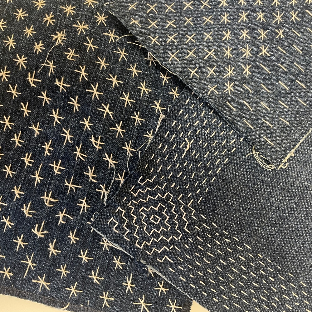 Flera tygbitar i blått med vita broderade mönster i olika geometriska former.