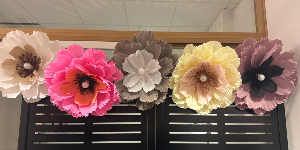 Fem stora, färgglada pappersblommor sitter fast på en svart skärm framför en spegel.