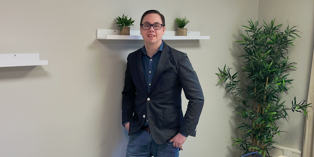 En person står vid väggen i ett mötesrum med bord, stolar, växter och hyllor med krukväxter.