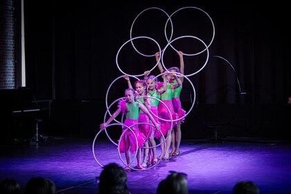 Fyra barn i gröna och rosa scenkläder uppträder med rockringar på en scen inför publik.