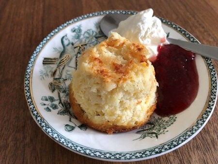 En tallrik med en kokosboll, vispad grädde och röd sylt på ett träbord.