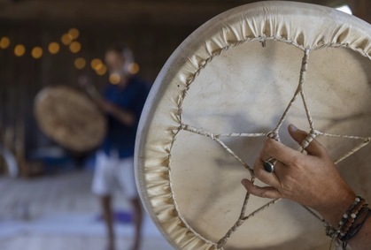 Närbild av en hand som håller en ramtrumma, suddig person i bakgrunden med en annan trumma.
